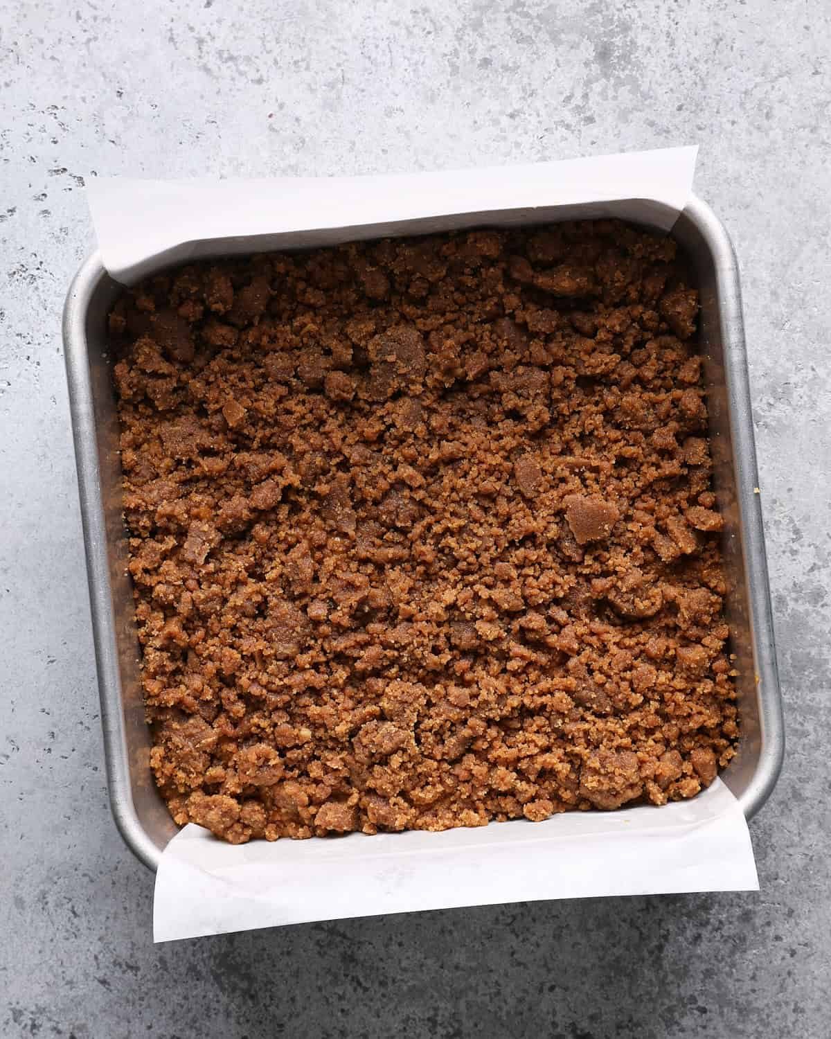 Unbaked pumpkin coffee cake in a parchment-lined square pan covered with crumb topping.