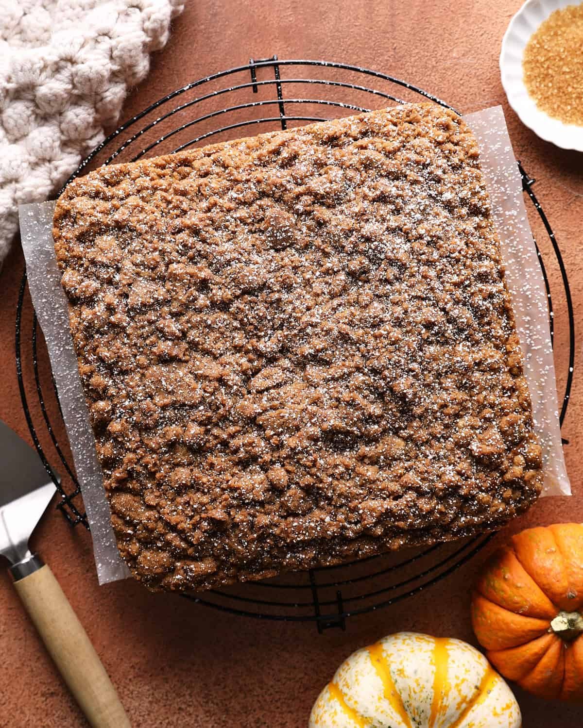Whole pumpkin coffee cake with a thick brown sugar crumb topping on a cooling rack.