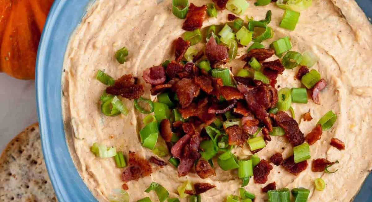 Overhead image of savory pumpkin and bacon dip with garnish in a blue bowl.