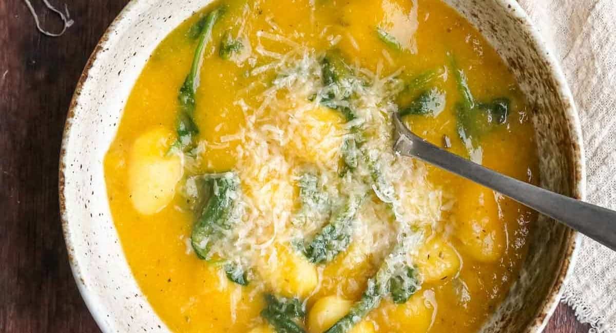 Overhead image of spicy & smoky pumpkin gnocchi soup in white bowl with spoon.