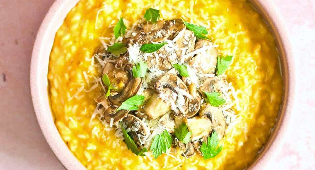 Overhead image of creamy pumpkin & mushroom risotto in bowl with garnish.