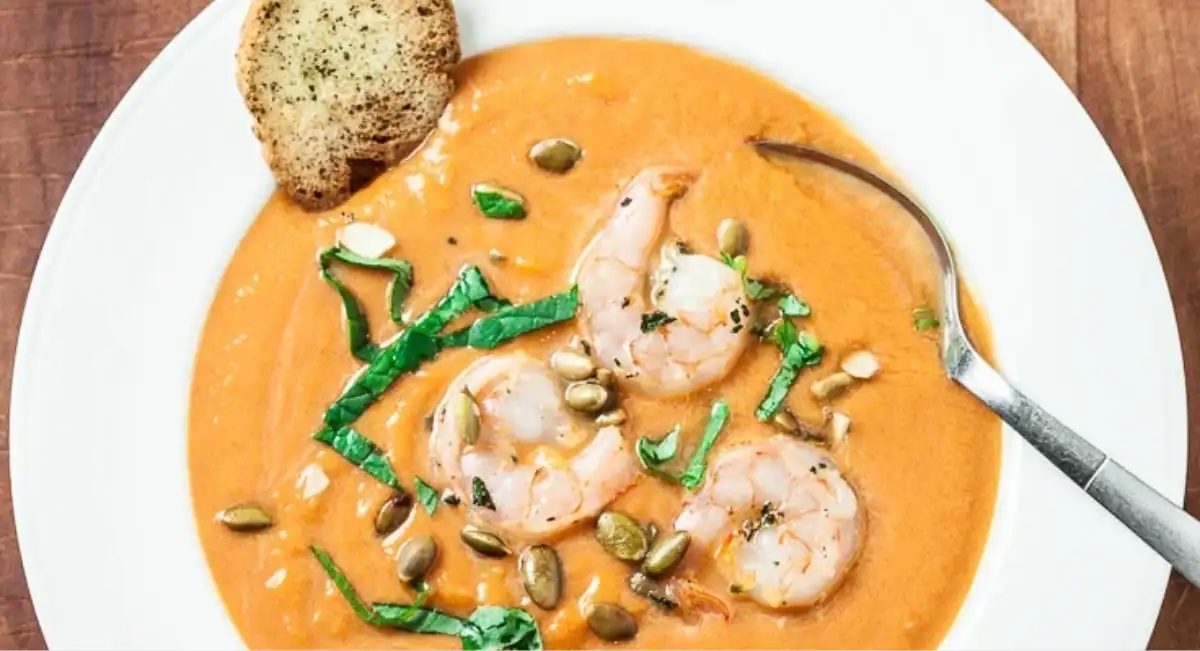 Overhead image of pumpkin shrimp bisque in white bowl with garnish.