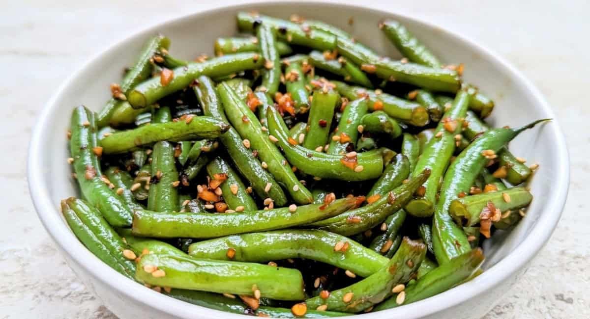 Overhead image of garlic sesame green beans with garnish in white bowl.