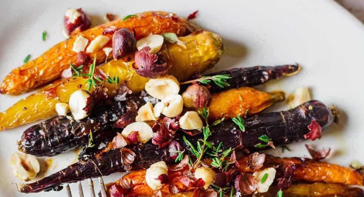 Overhead image of roasted carrots with hazelnuts and garnish.