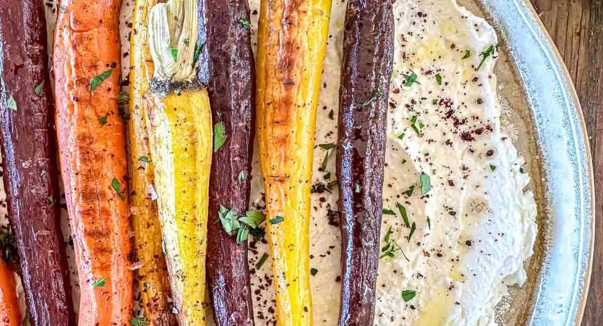 Overhead image of roasted rainbow carrots with whipped feta and garnish.