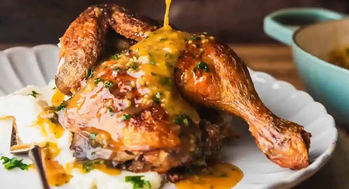 Up close image of roasted half chicken with garnish on white dish.