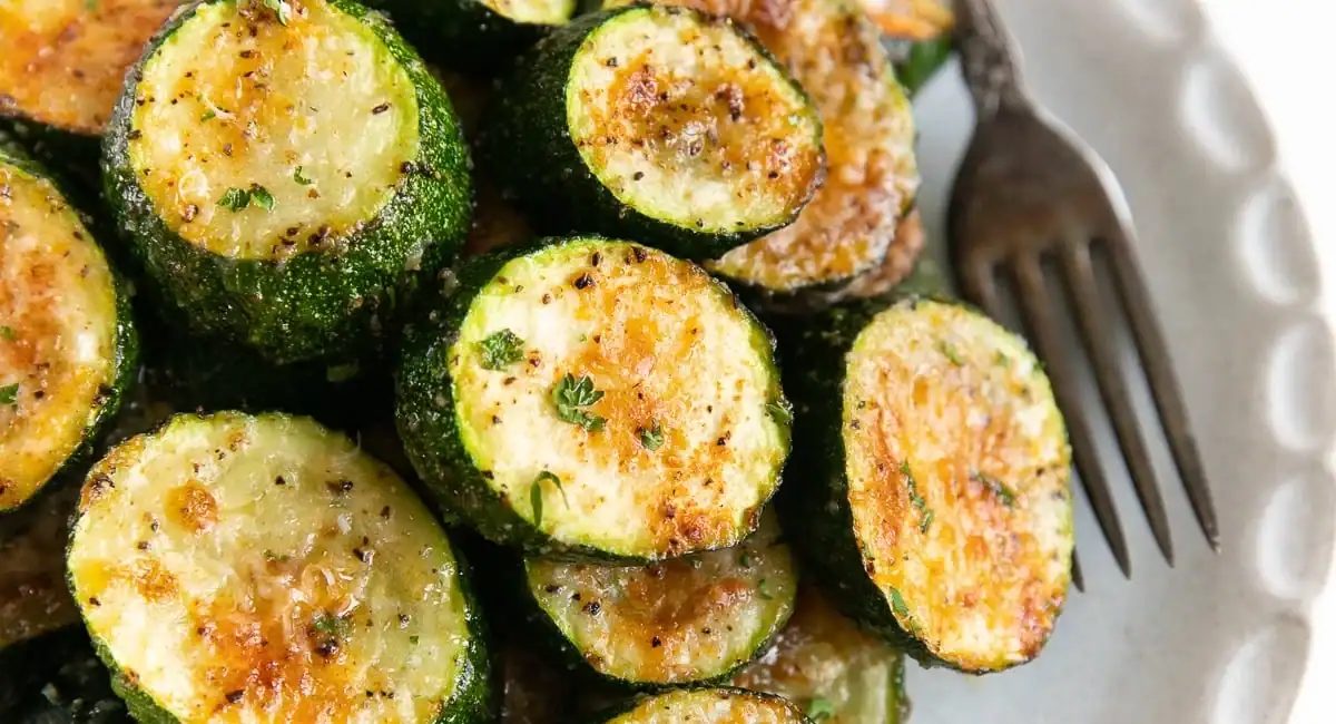 Up close image of roasted zucchini with parmesan on white plate.