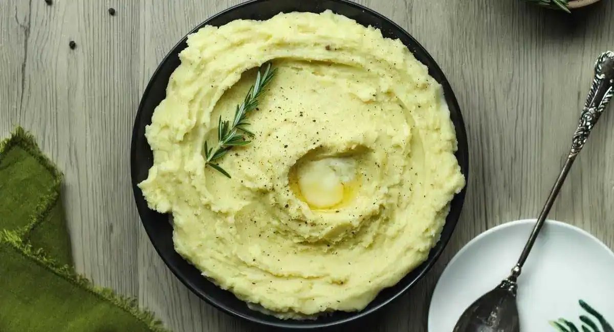 Overhead image of rosemary garlic mashed potatoes in black bowl with garnish.