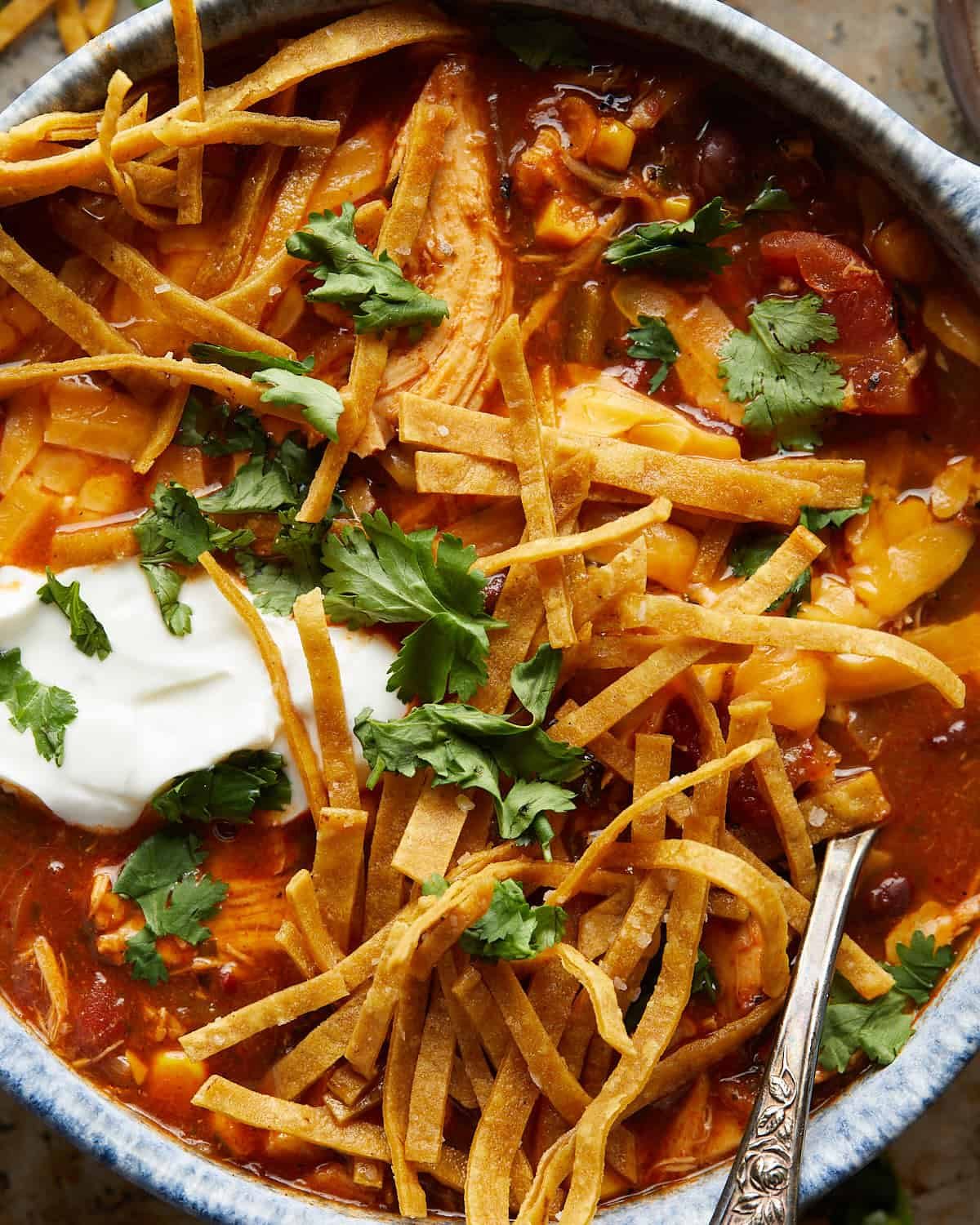 Overhead up close image of chicken tortilla soup with tortilla strips and garnish.