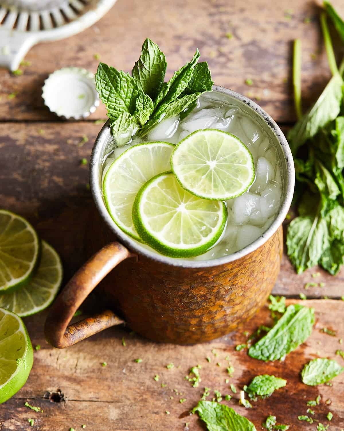 3/4 shot of rum moscow mule in a copper mug with limes and mint leaves on top.