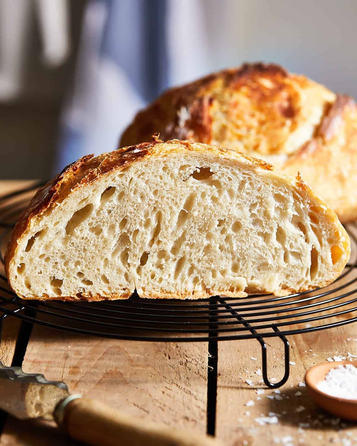 Sliced rustic bread on a cooling rack showing an airy, irregular crumb and crisp golden-brown crust.