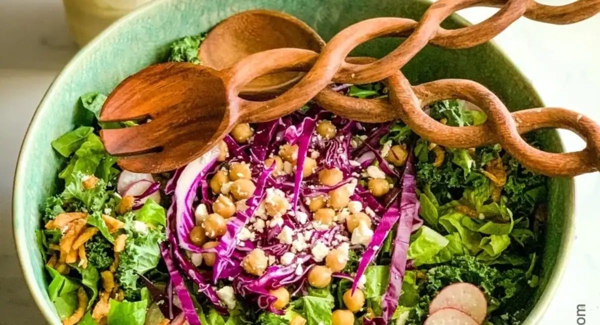 Overhead image of kale crunch salad in green bowl with wooden spoon and salad fork.
