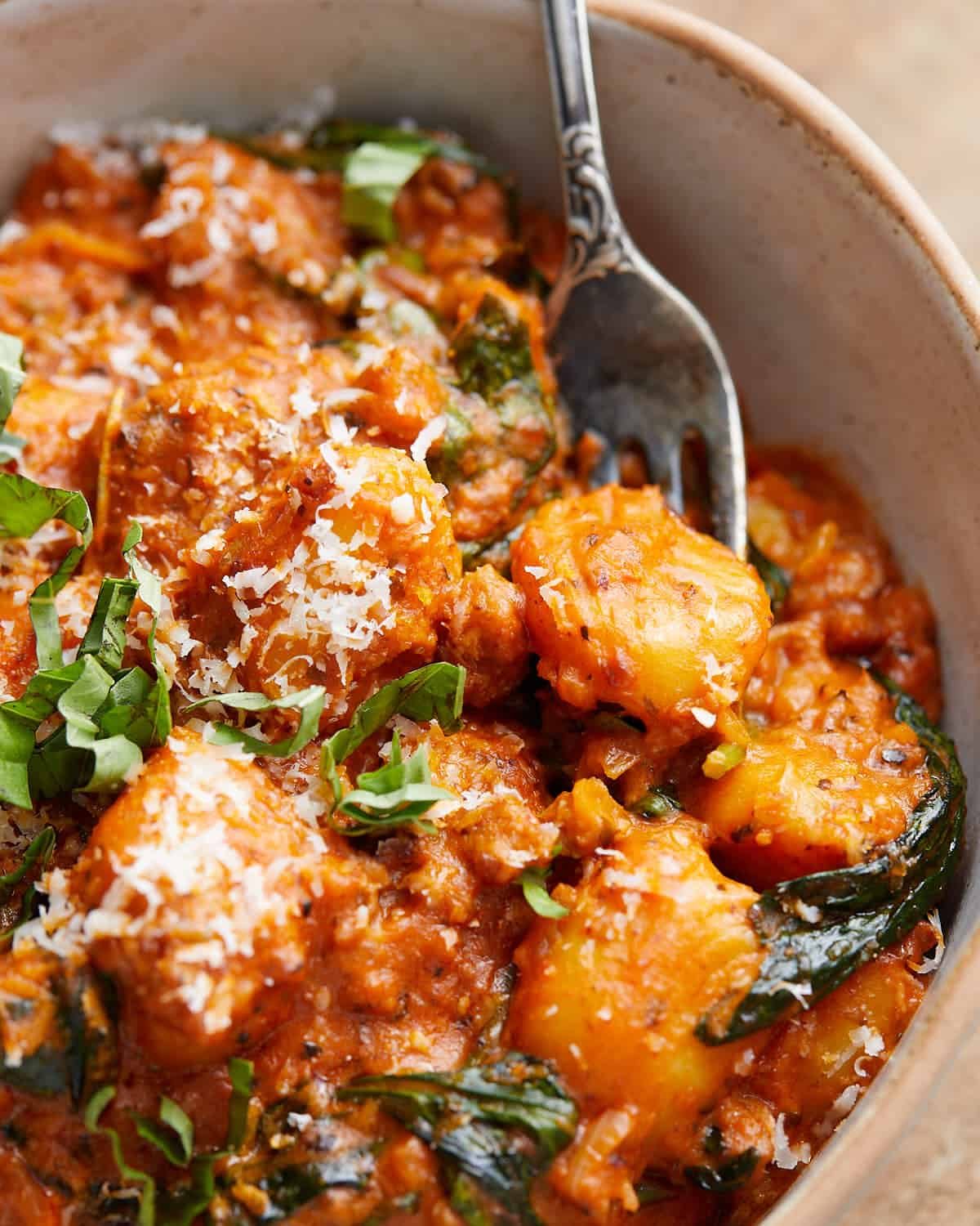 Up close image of sausage gnocchi with creamy tomato sauce and spinach.