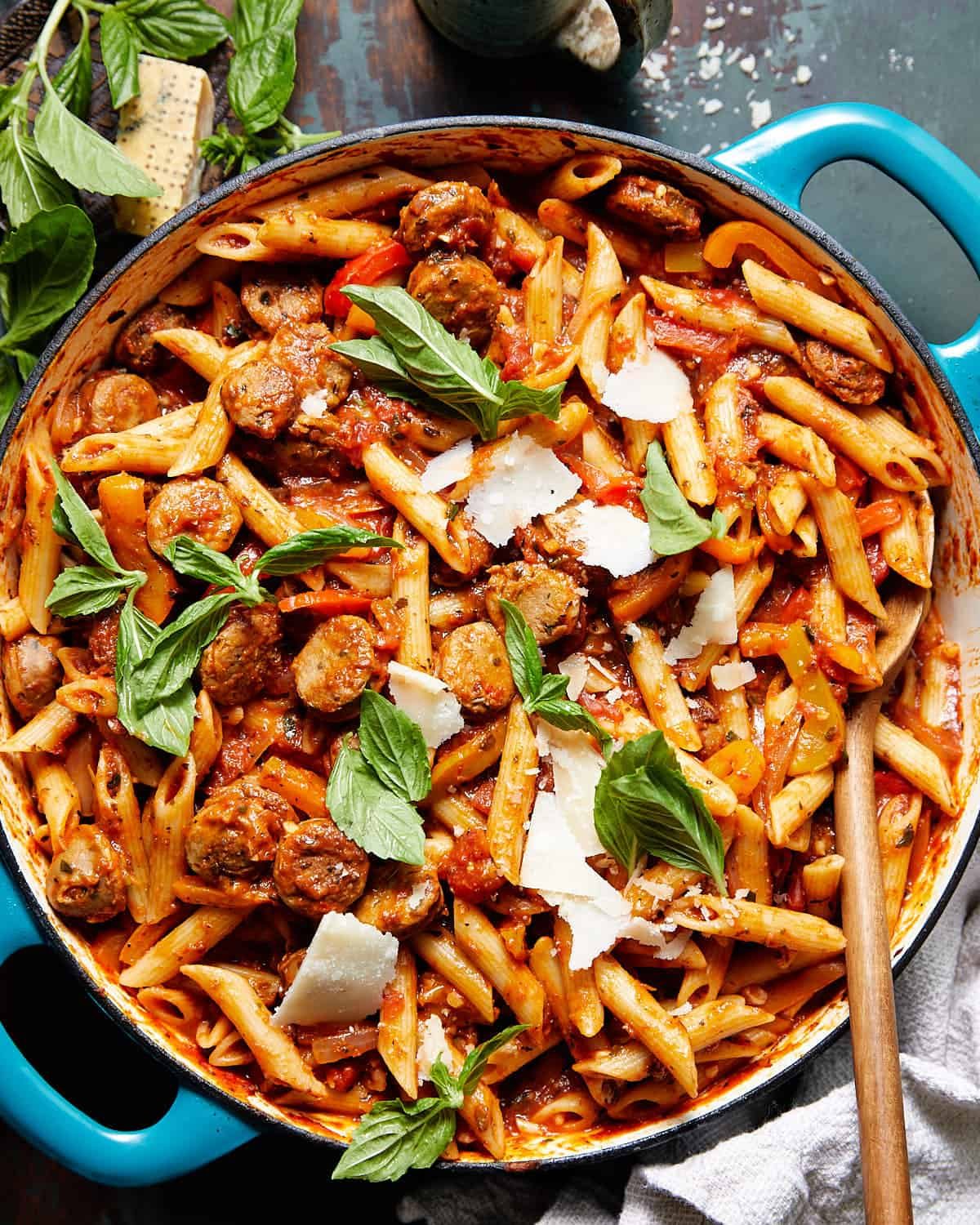 Sausage and peppers pasta with basil and parmesan in a blue pot.