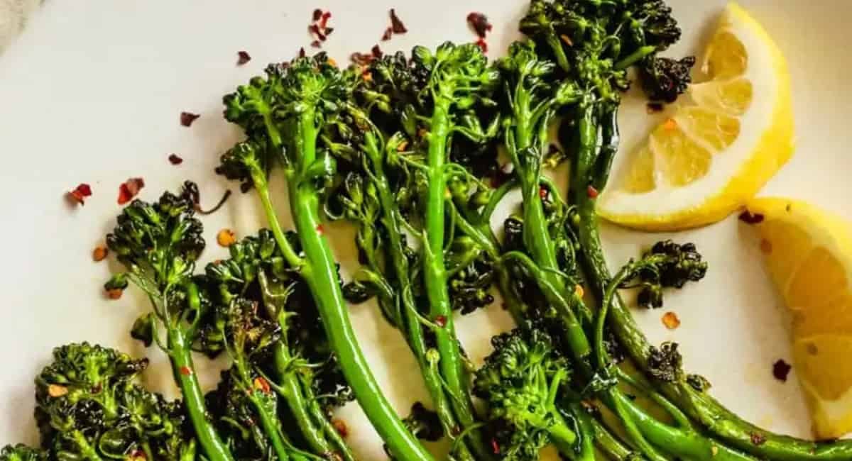Broccolini served on a white plate as a side for meatball subs.