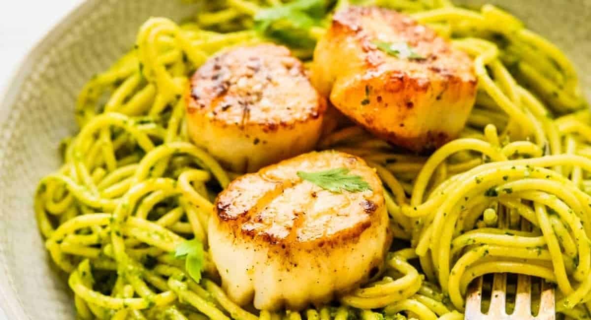 Up close image of pan seared scallops over spinach pesto pasta.