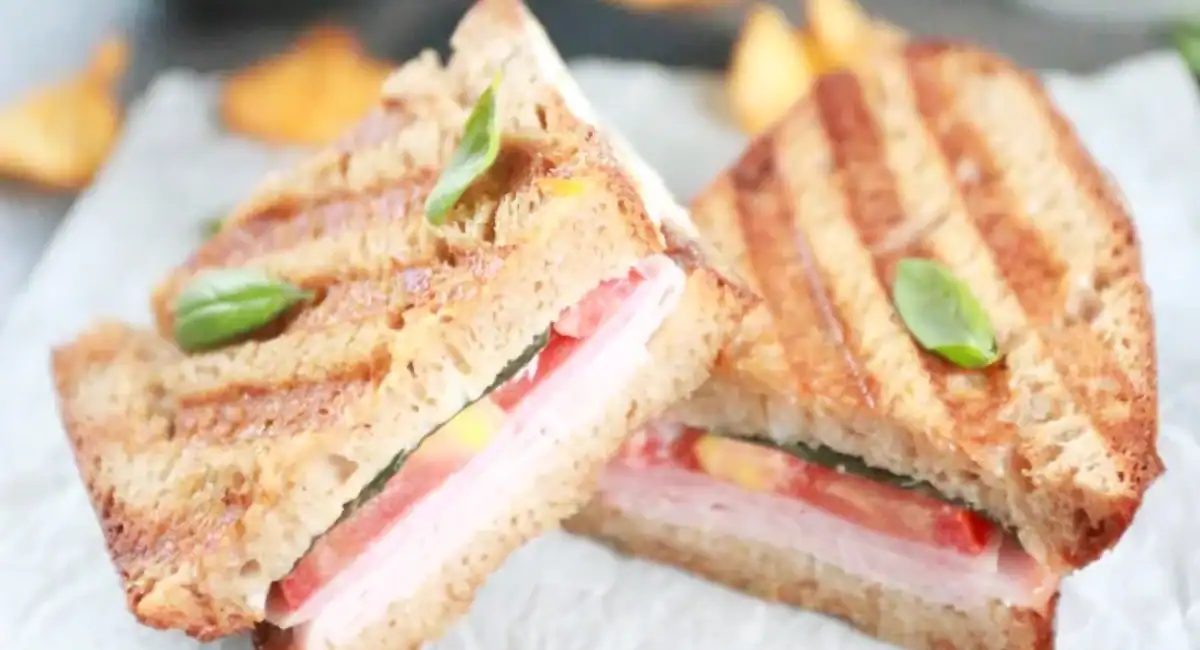 Up close image of panini sandwich with ham and tomatoes cut in half.