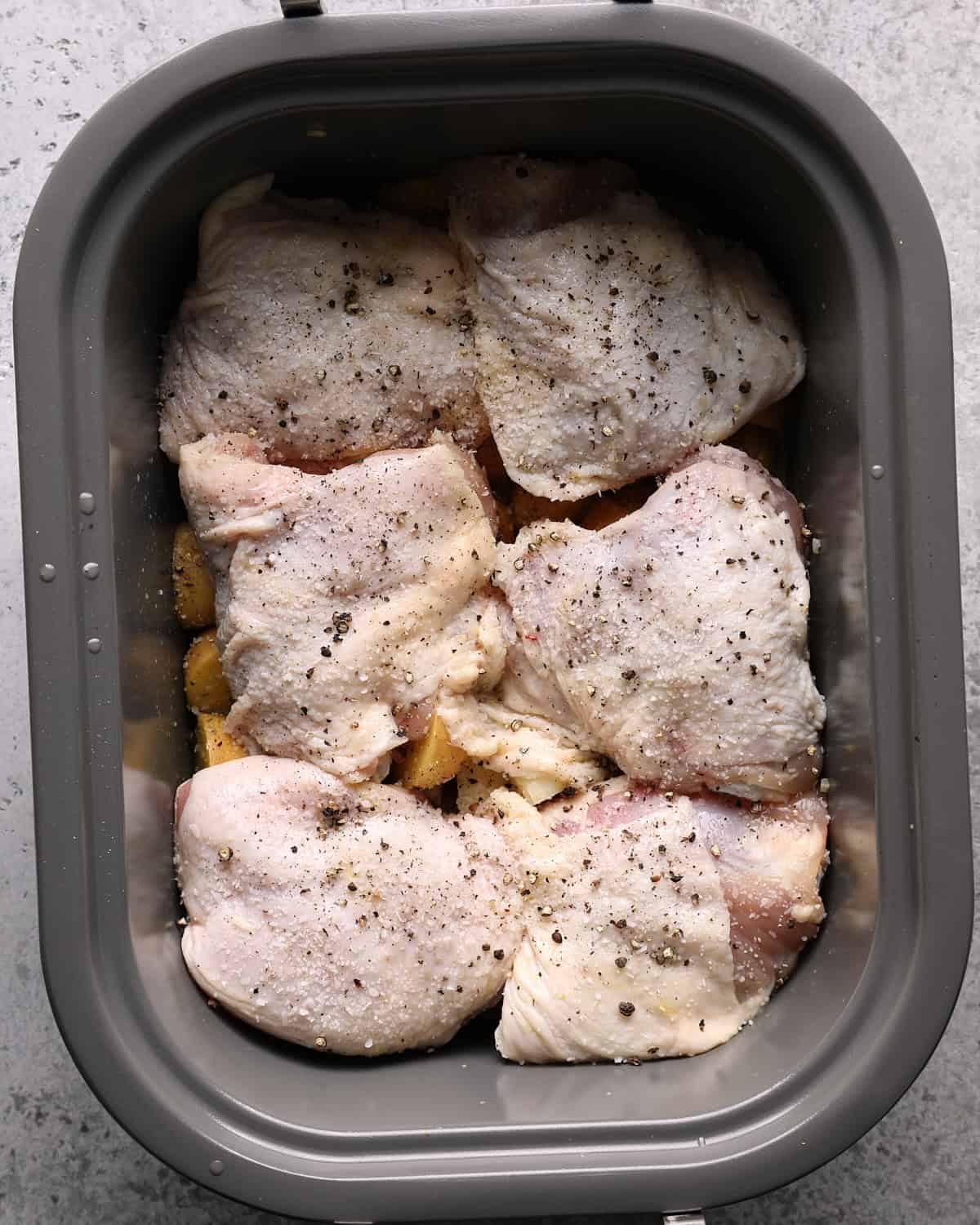 Raw bone-in chicken thighs arranged skin-side up over potatoes in a slow cooker.