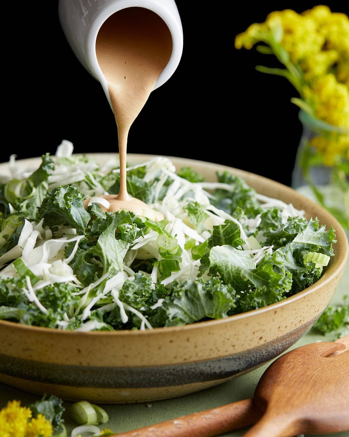 Spicy cashew dressing being poured over salad mix.