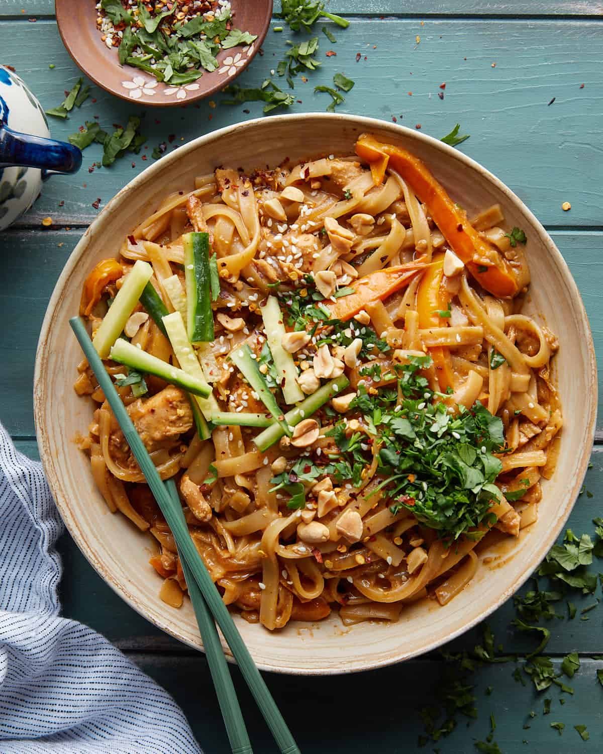 Overhead image of spicy peanut noodles with chicken in beige bowl.