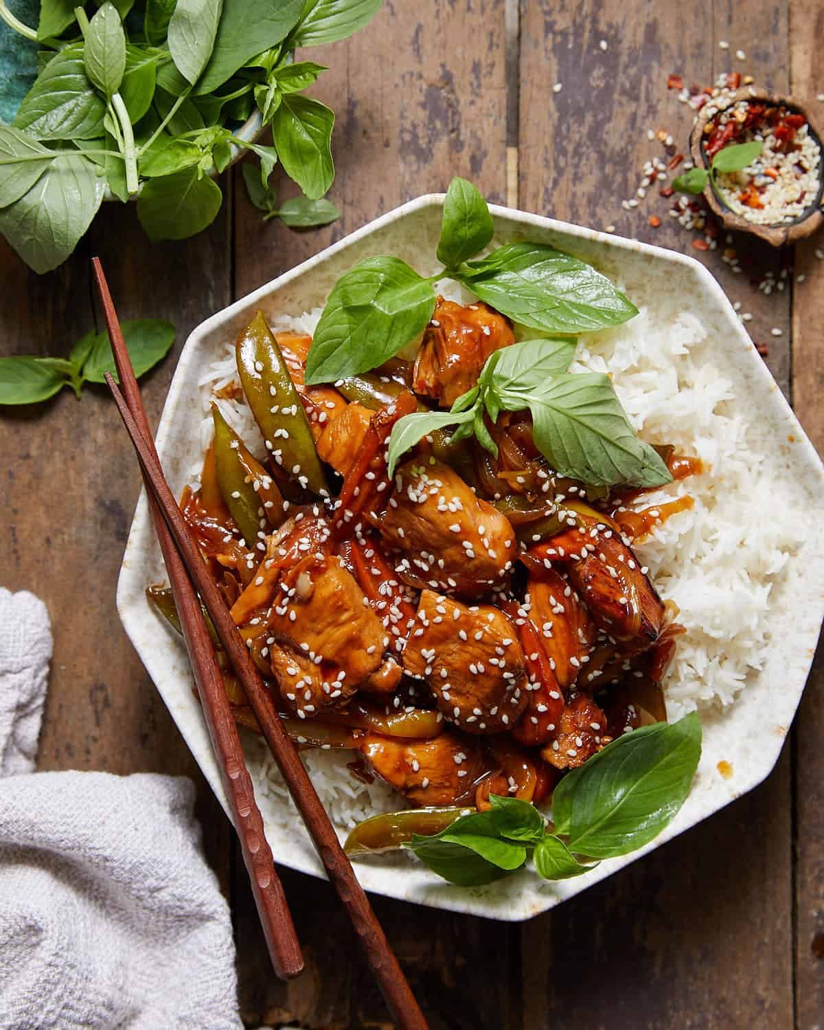 Stir fry marinated chicken and veggis over rice in a bowl.