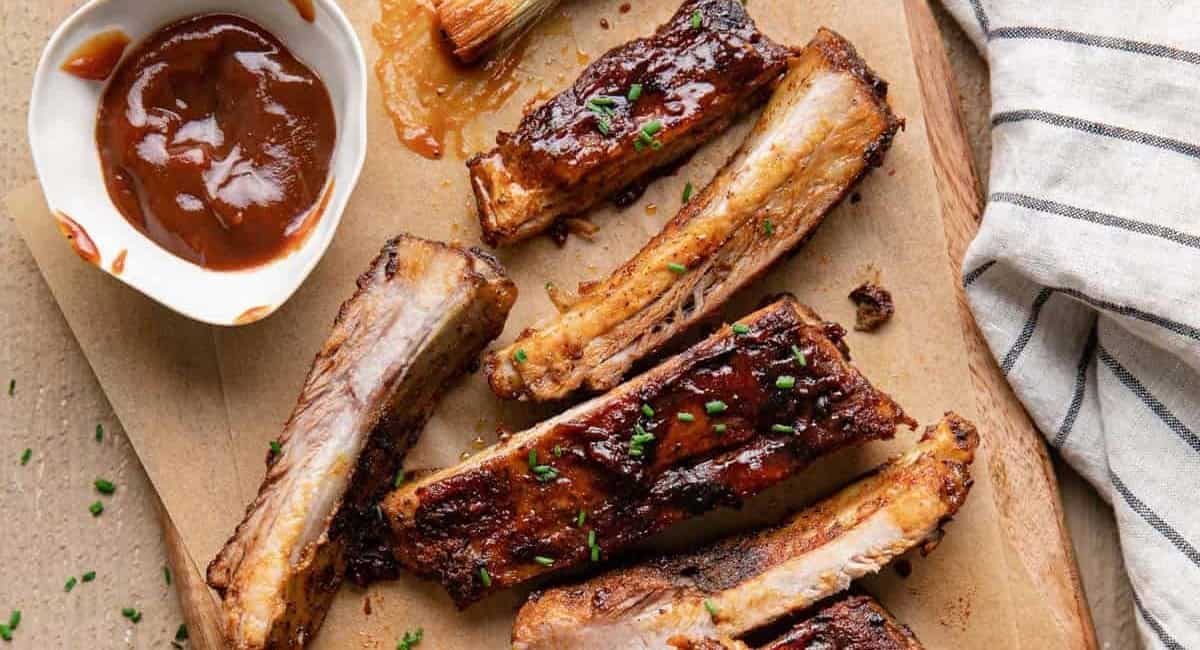 Overhead image of bbq St. Louis ribs on wooden board with bbq sauce on the side.