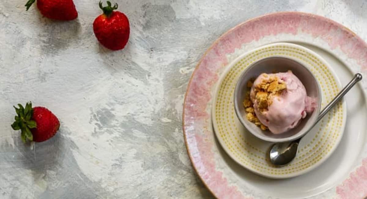 Strawberry cheesecake ice cream served in a white bowl on a pink plate.