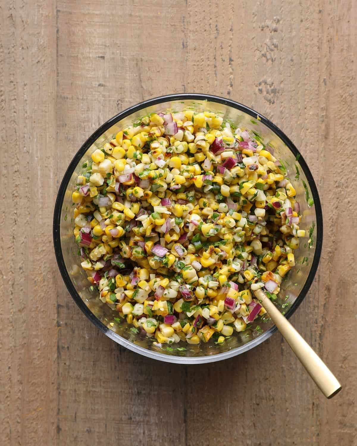 Corn salsa mixed with charred corn, jalapeño, red onion, cilantro, lime juice, and salt.