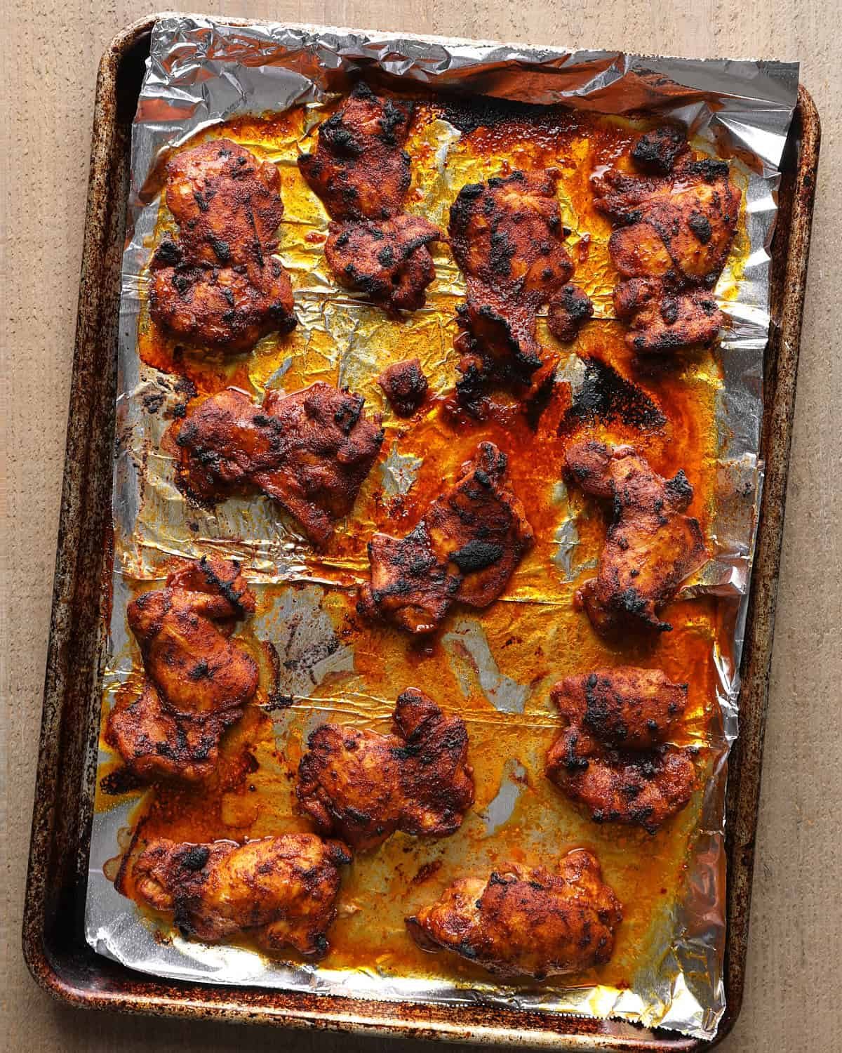 Broiled chicken thighs on a foil-lined sheet pan, charred on top.