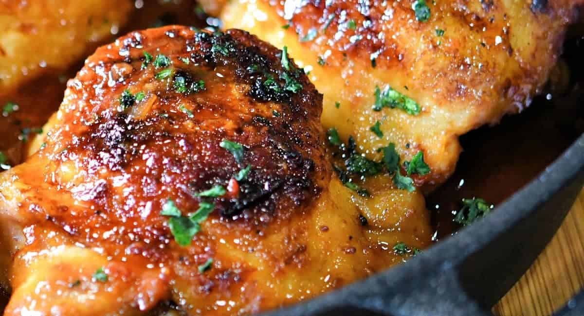 Up close overhead image of sweet and spicy chicken thighs in cast iron skillet.
