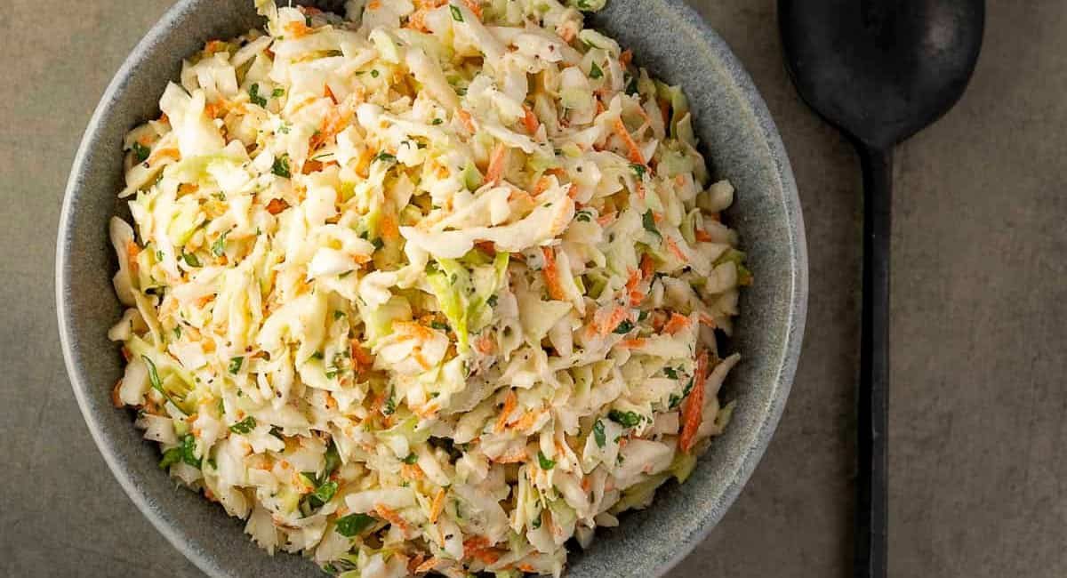Overhead image of Texas-style coleslaw in blue bowl with black spoon beside it.