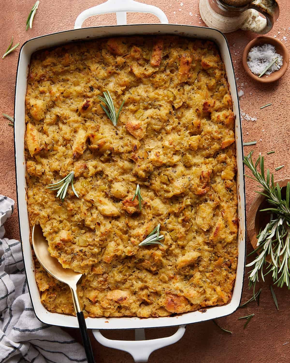 Overhead image of make ahead stuffing baked in a white casserole dish, featuring golden toasted bread cubes, herbs, and a crisp buttery topping.