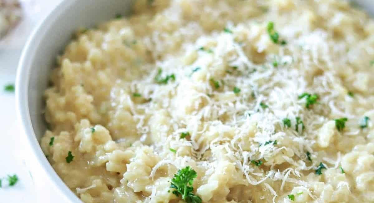 Overhead image of creamy garlic parmesan risotto with garnish in white bowl.