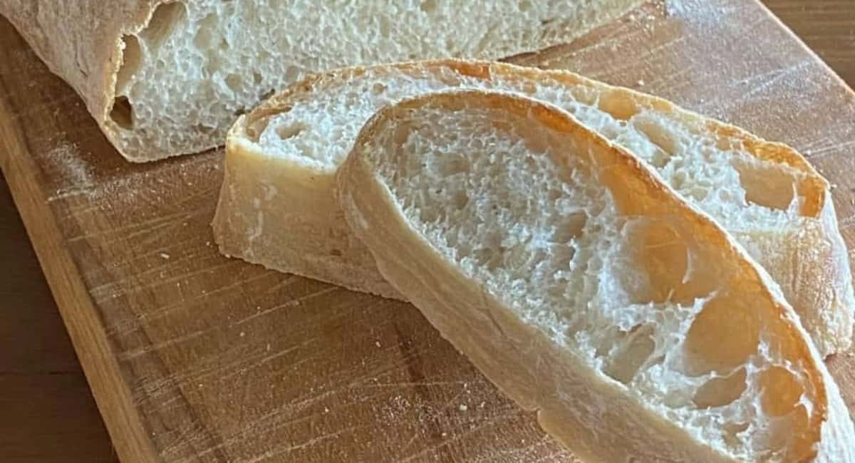 Up close overhead image of artisan ciabatta bread on wooden cutting board.