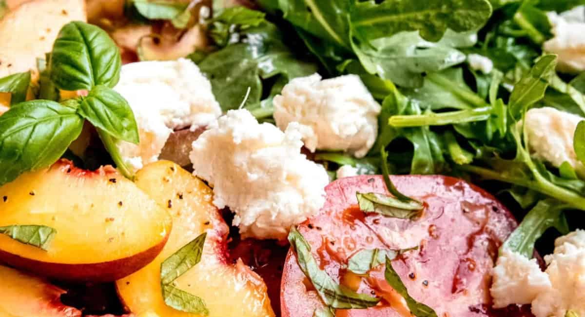 Up close overhead image of peach caprese with tomatoes, burrata, arugula, and white balsamic vinaigrette.