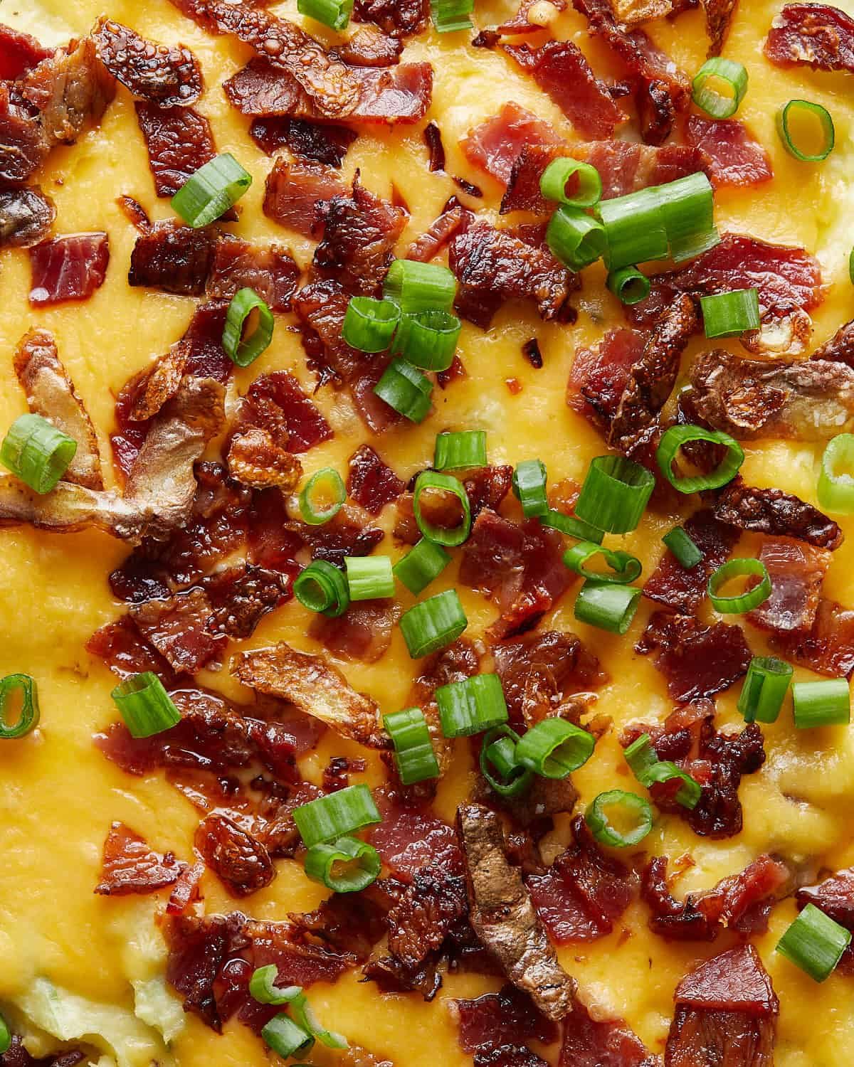 Up close image of twice-baked mashed potatoes with bacon, green onions, crispy potato peels and cheddar cheese topping.