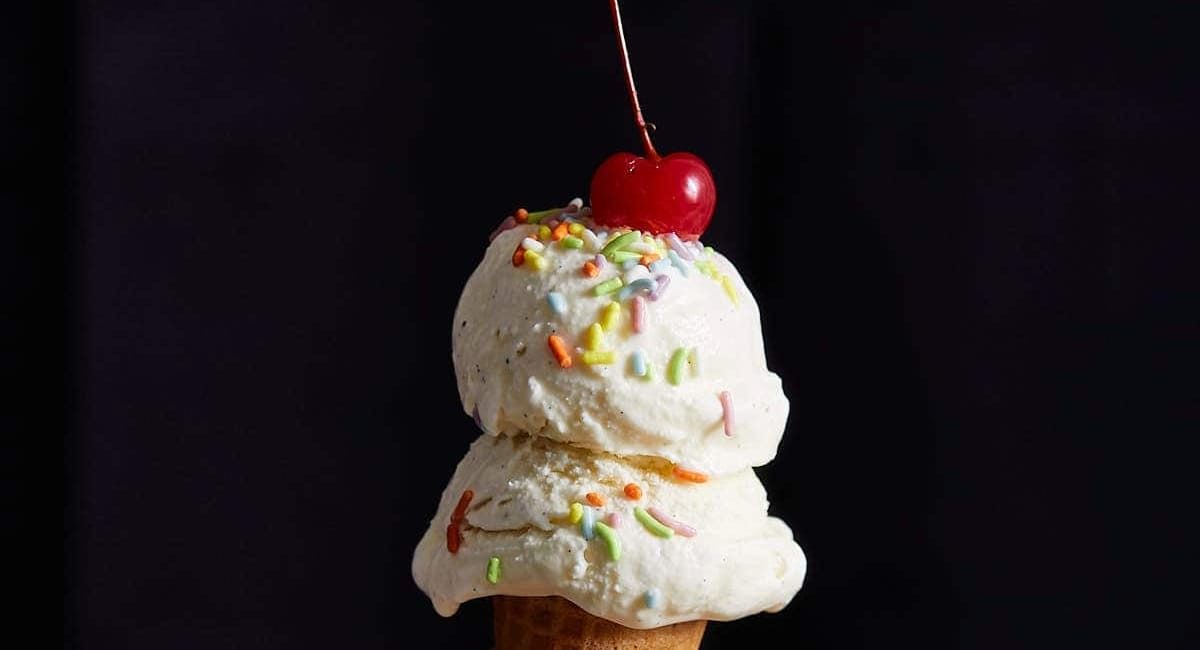 Up close image of no egg vanilla ice cream with sprinkles and a cherry on top.