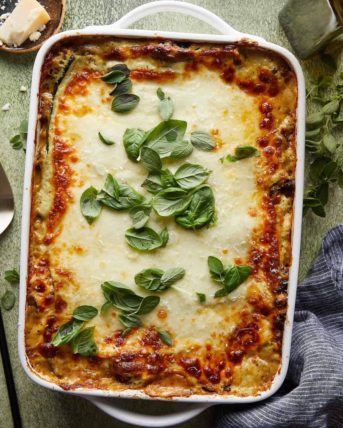 Overhead image of veggie lasagna with white sauce and garnish.