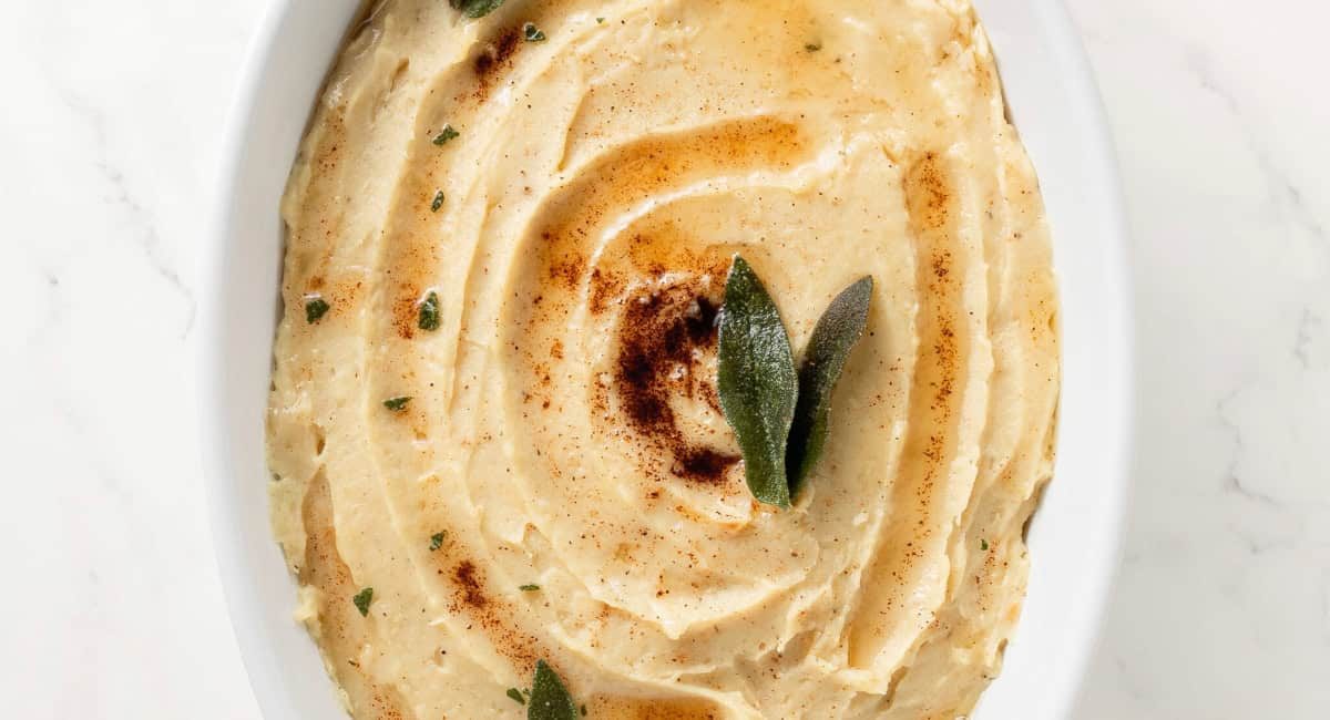 Overhead image of mashed white sweet potatoes with brown butter and garnish.