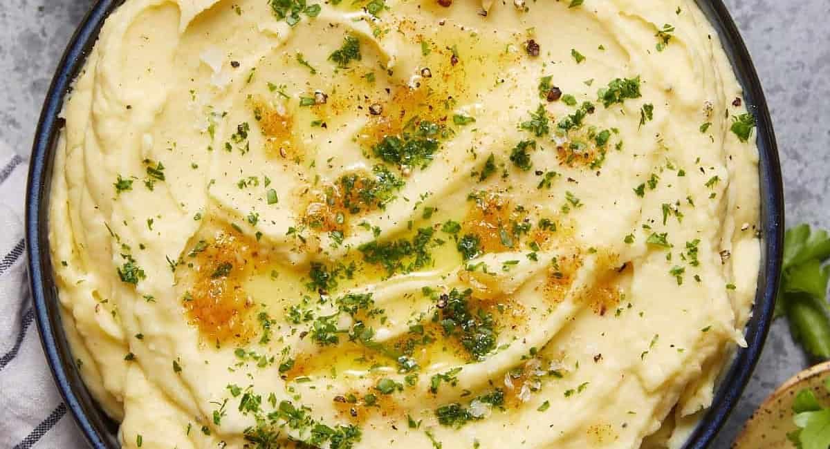 Overhead image of yukon gold mashed potatoes with garnish in black bowl.
