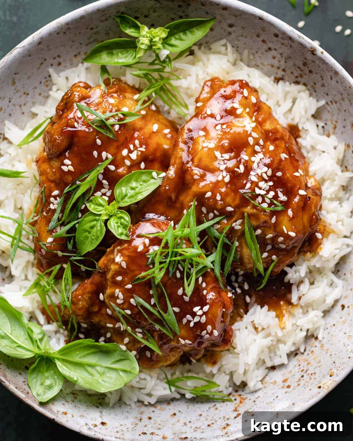 Easy Air Fryer Teriyaki Chicken 6 Air fryer teriyaki chicken thighs over rice. Close-up of crispy teriyaki chicken thigh garnished with sesame seeds and green onions, resting on a bed of white rice.