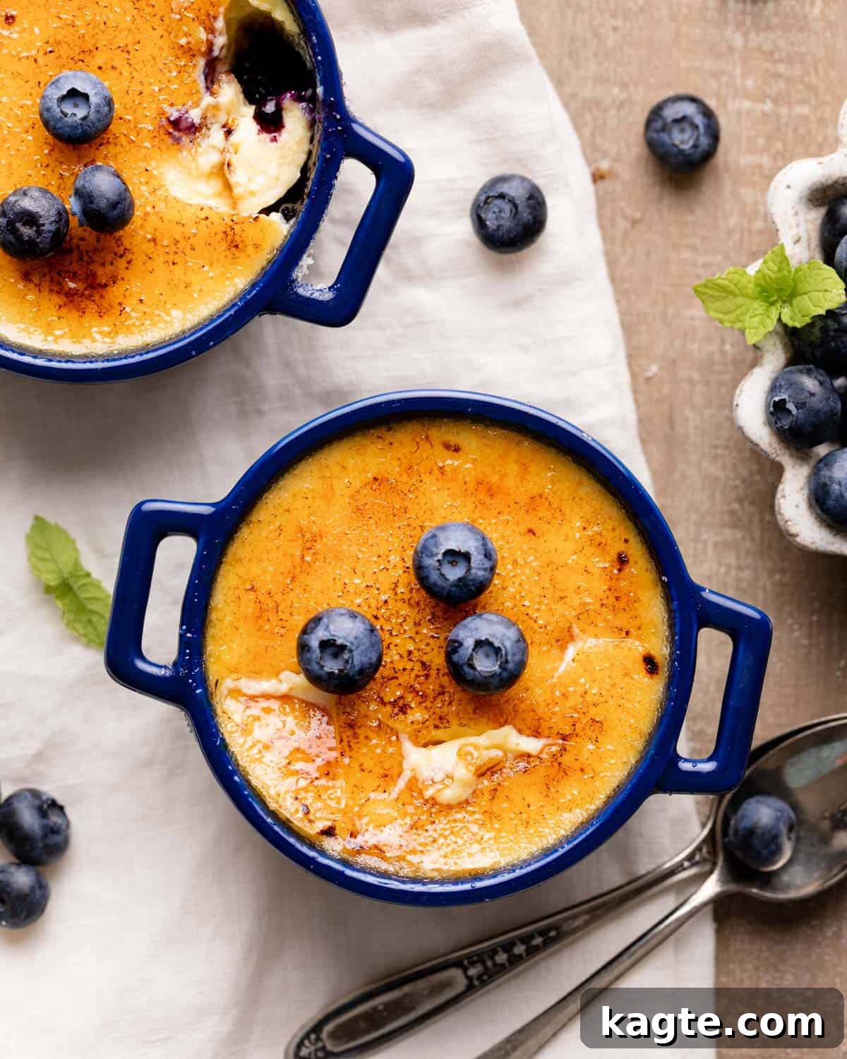 Double Delight Blueberry Crème Brûlée 2 Two ramekins of Blueberry Crème Brûlée with a golden caramelized sugar topping, garnished with fresh blueberries.