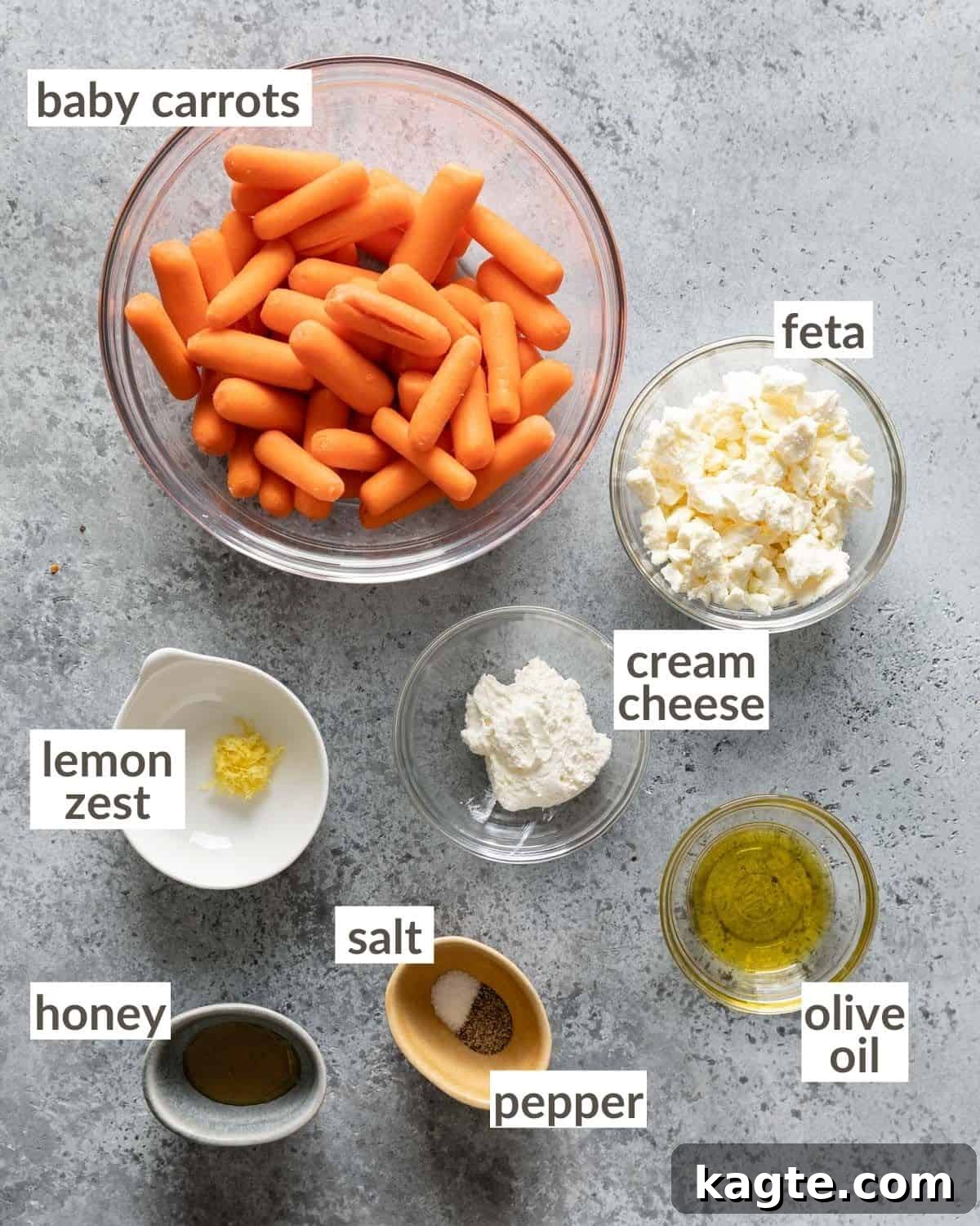Overhead view of various ingredients in small bowls, including fresh baby carrots, olive oil, honey, feta cheese, and lemon, prepared for the air fryer baby carrots recipe.