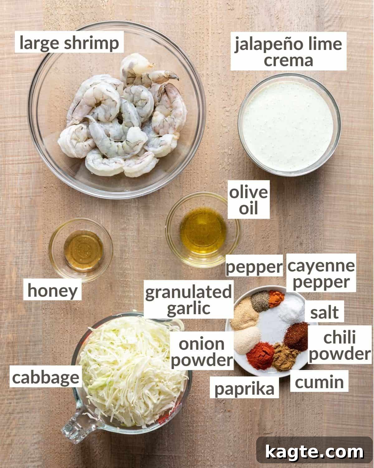 Overhead image of all fresh ingredients needed to make air fryer shrimp tacos, including raw shrimp, various spices, fresh cabbage, limes, and olive oil, laid out on a clean surface.