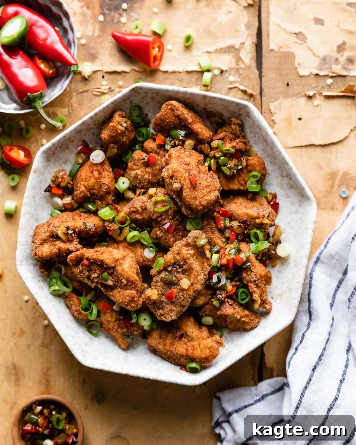 Overhead view of crispy salt and pepper chicken served in a bowl, garnished with fresh chilis and scallions
