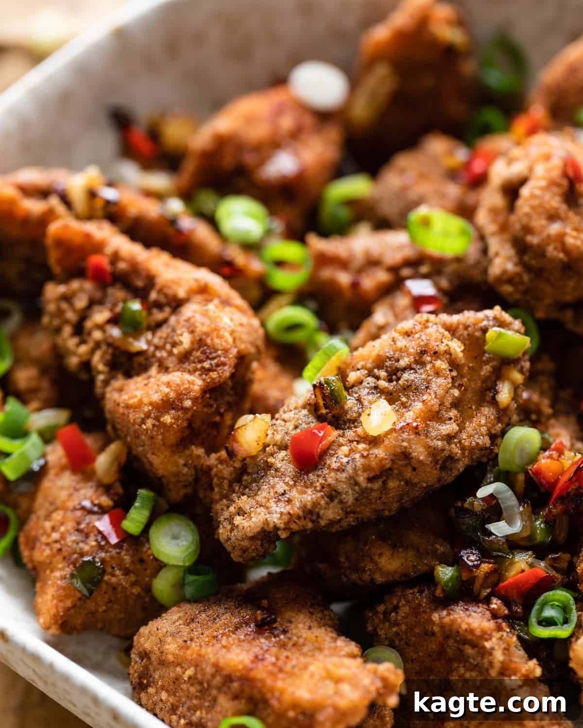 Close-up of crispy salt and pepper chicken garnished with fresh chilis, garlic, and scallions