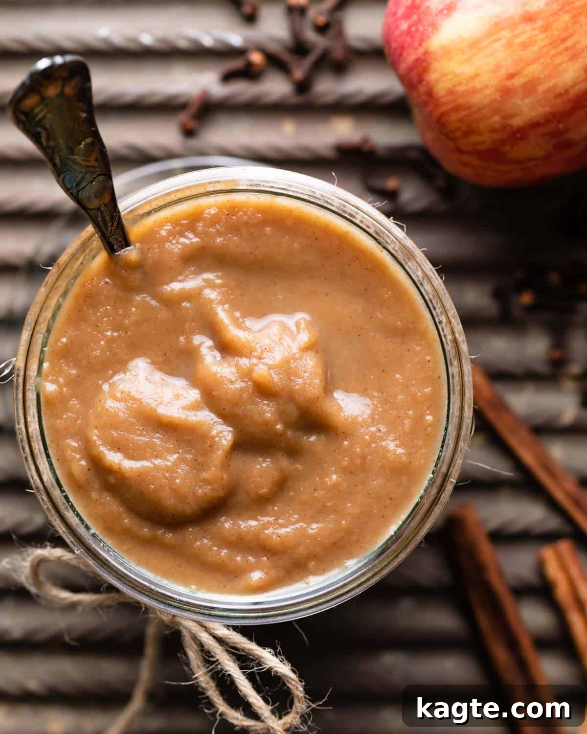 Luscious Apple Curd 2 A jar filled with homemade apple curd, accompanied by fresh apples and cinnamon sticks, with a spoon nestled inside.
