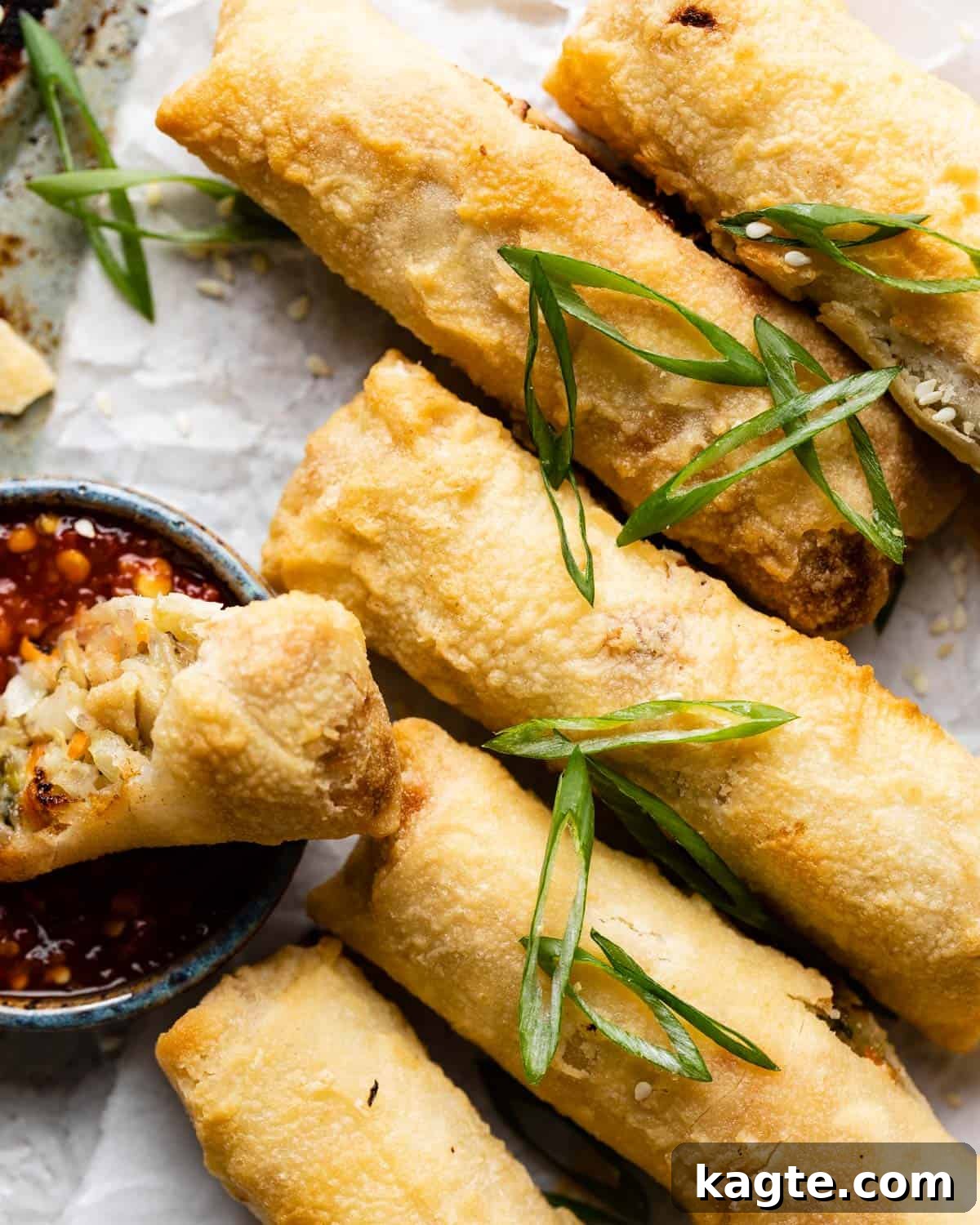 Crispy Air Fried Frozen Egg Rolls 5 Up close image of air fryer egg rolls with green onion and sesame seed garnish, next to a bowl of dipping sauce.