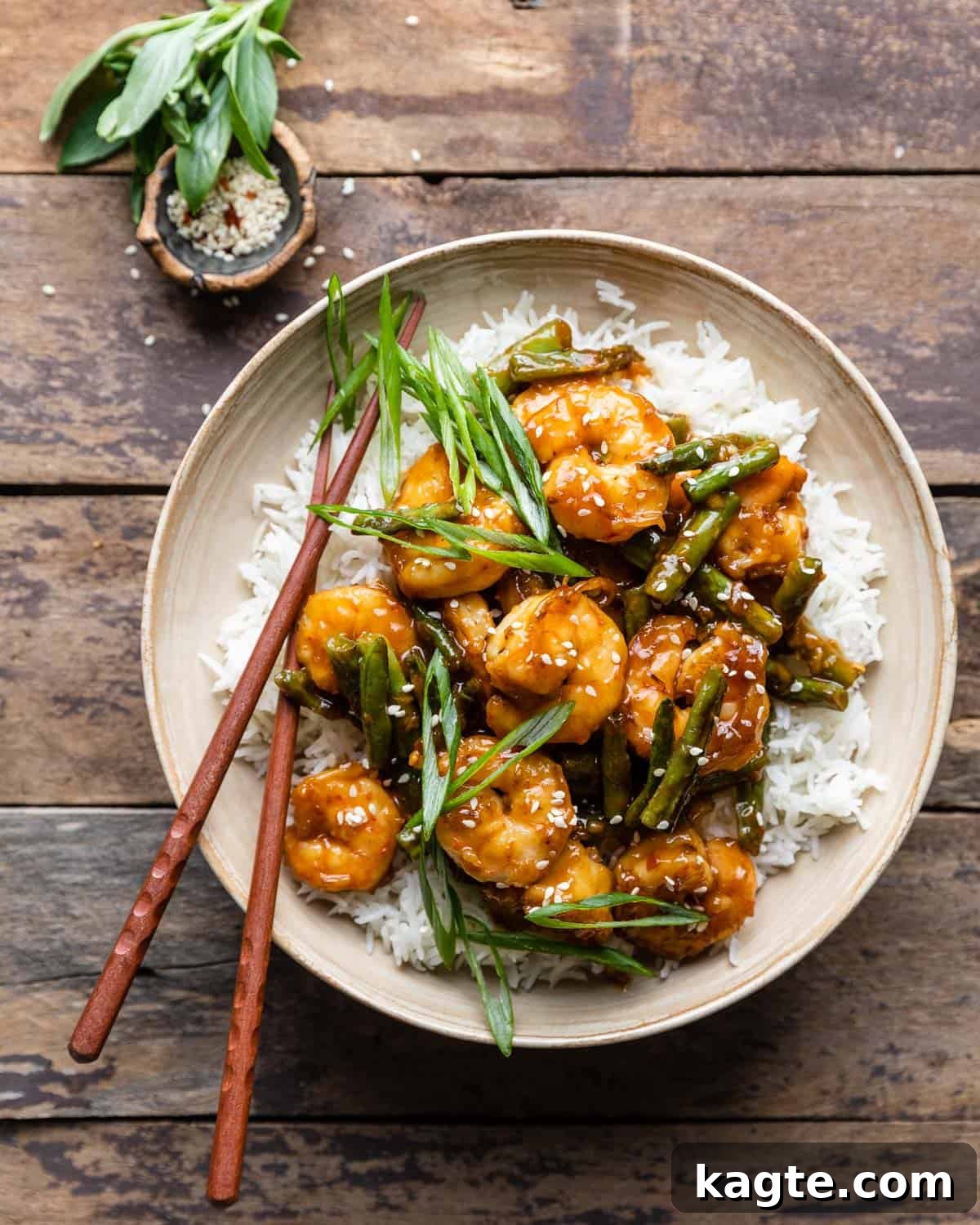 Cream colored bowl with hunan shrimp and white rice with scallions on top. 