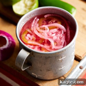 A close-up of Mexican pickled onions in a glass jar, showcasing their vibrant pink color and delicate slices.